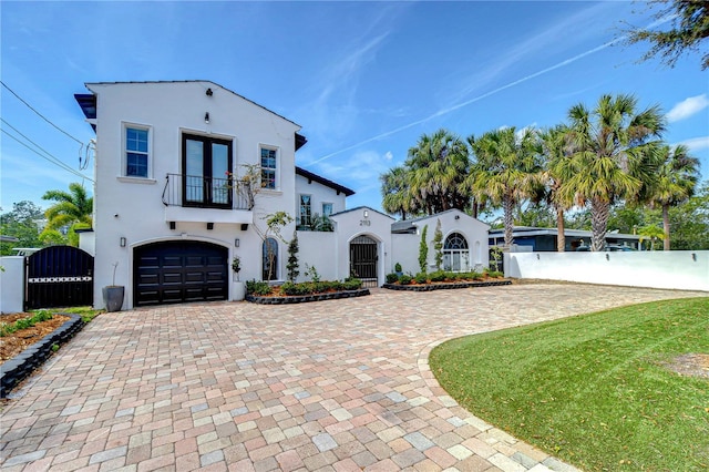 mediterranean / spanish home with stucco siding, an attached garage, a gate, fence, and a balcony