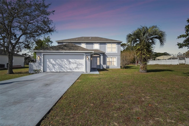 traditional-style house featuring an attached garage, fence, driveway, stucco siding, and a front lawn