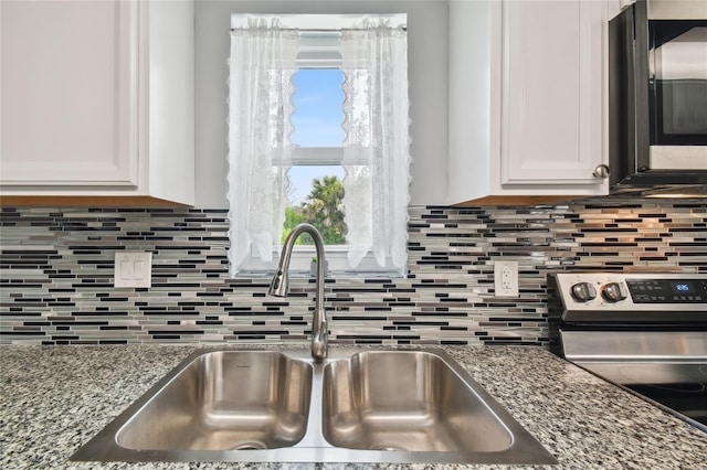 kitchen with sink, stone counters, white cabinetry, appliances with stainless steel finishes, and decorative backsplash