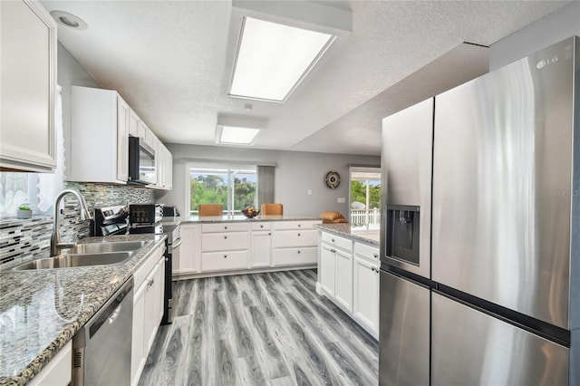 kitchen with sink, stainless steel appliances, light stone countertops, white cabinets, and decorative backsplash