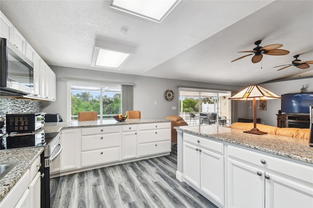 kitchen featuring appliances with stainless steel finishes, white cabinets, decorative backsplash, light hardwood / wood-style floors, and light stone countertops