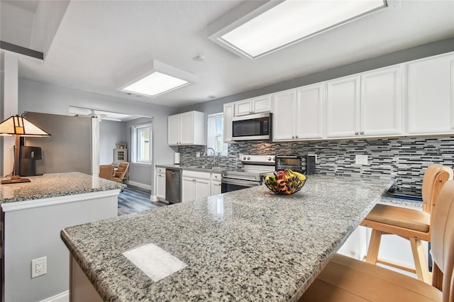 kitchen with a kitchen island, a breakfast bar, white cabinets, stainless steel appliances, and light stone countertops