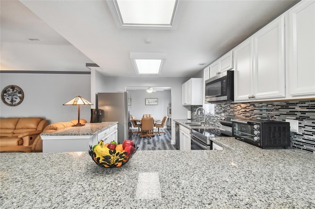 kitchen featuring light stone countertops, stainless steel appliances, kitchen peninsula, and white cabinets