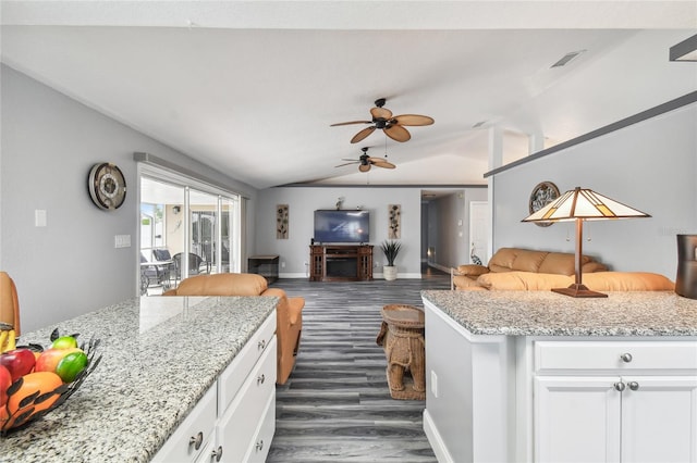 kitchen featuring dark wood-type flooring, ceiling fan, white cabinetry, light stone counters, and vaulted ceiling