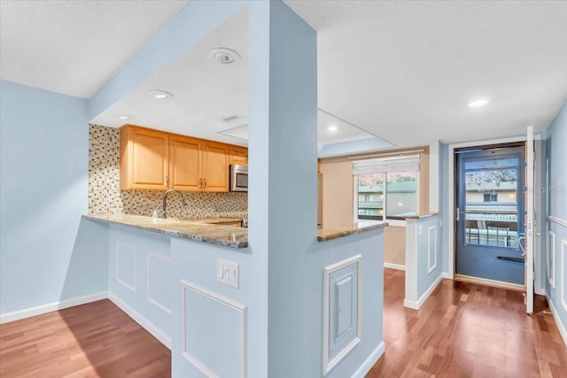 kitchen with tasteful backsplash, light stone countertops, sink, and hardwood / wood-style floors