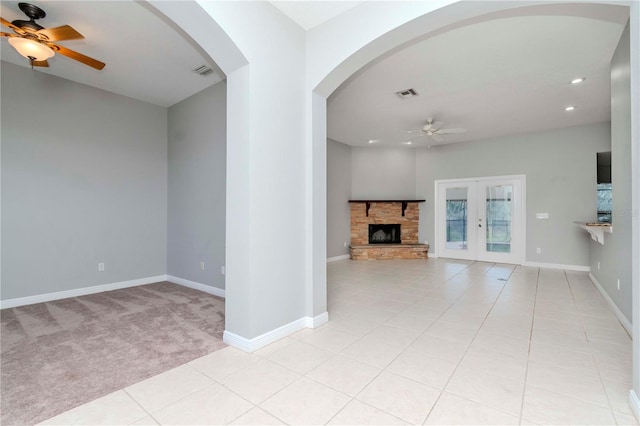 unfurnished living room featuring light tile patterned flooring, ceiling fan, a stone fireplace, and french doors