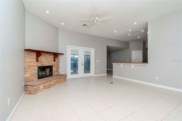 unfurnished living room featuring light tile patterned flooring, a stone fireplace, ceiling fan, and french doors