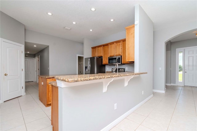 kitchen featuring light tile patterned floors, appliances with stainless steel finishes, a kitchen breakfast bar, kitchen peninsula, and light stone countertops