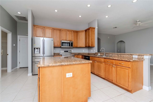 kitchen featuring sink, appliances with stainless steel finishes, kitchen peninsula, a kitchen island, and light stone countertops