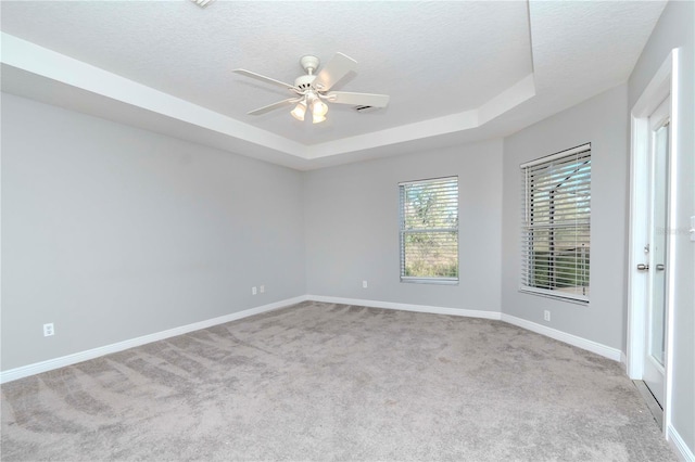 unfurnished room with ceiling fan, a raised ceiling, light carpet, and a textured ceiling