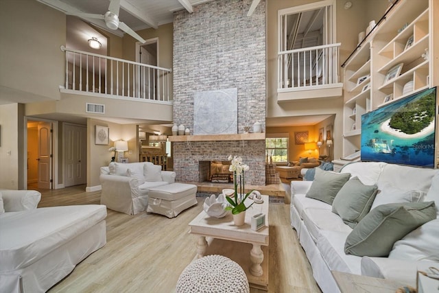 living room with beamed ceiling, a towering ceiling, a fireplace, and light wood-type flooring