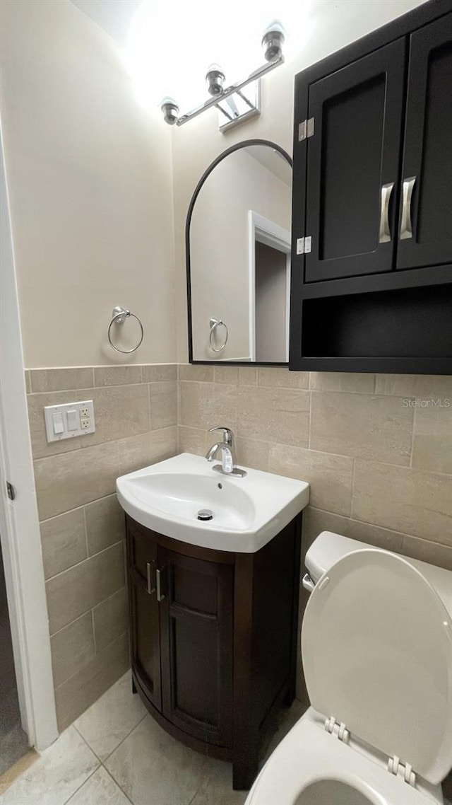 bathroom featuring tile patterned floors, vanity, toilet, and tile walls