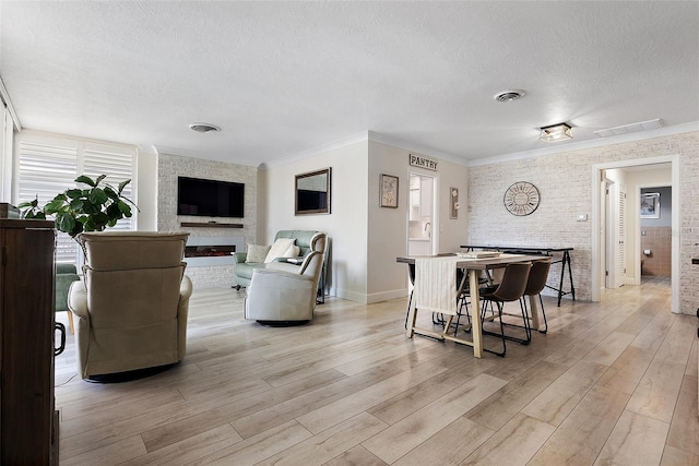 living room with light wood finished floors, visible vents, a textured ceiling, and ornamental molding