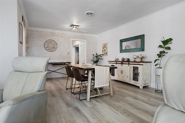 dining space with light wood-type flooring, brick wall, visible vents, and ornamental molding