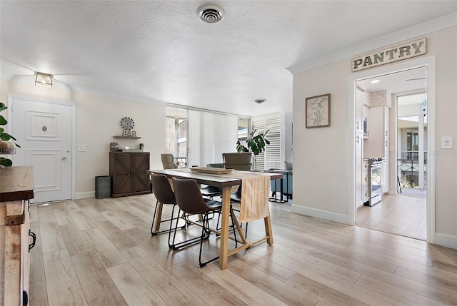 dining room featuring baseboards, visible vents, light wood-style flooring, and a textured ceiling