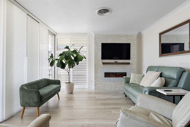 living room featuring ornamental molding, light wood-style flooring, a fireplace, and visible vents