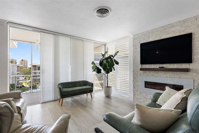 living area featuring a textured ceiling, a large fireplace, wood finished floors, visible vents, and a wall of windows