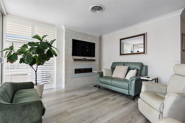 living area with light wood-type flooring, a brick fireplace, visible vents, and ornamental molding