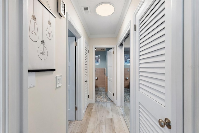 corridor featuring ornamental molding, light wood-type flooring, and visible vents