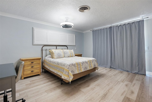 bedroom featuring ornamental molding, light wood-type flooring, visible vents, and a textured ceiling