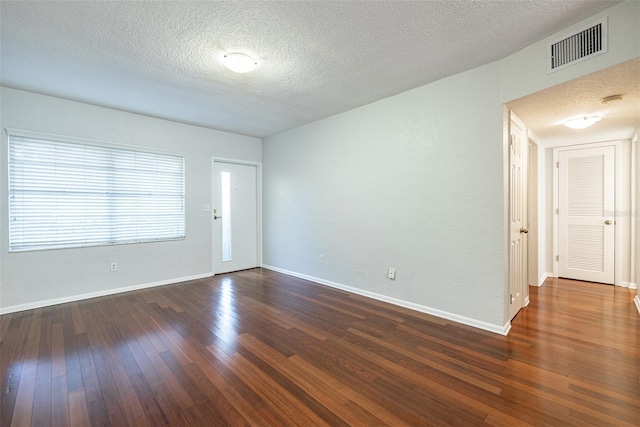 spare room with wood-type flooring, visible vents, a textured ceiling, and baseboards