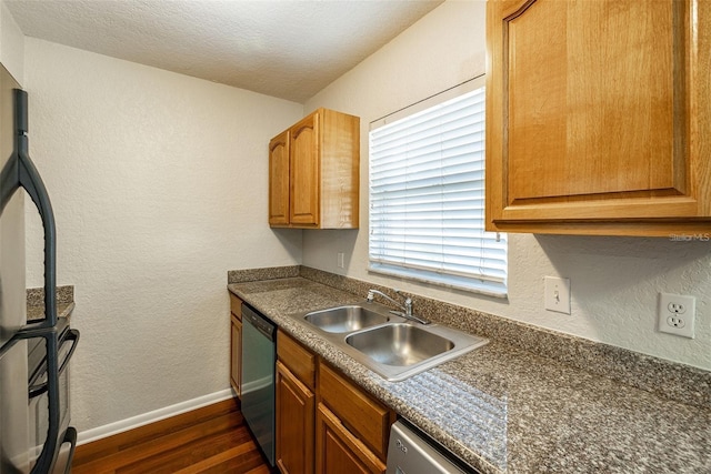 kitchen featuring dark wood-style flooring, a sink, baseboards, dishwasher, and dark countertops