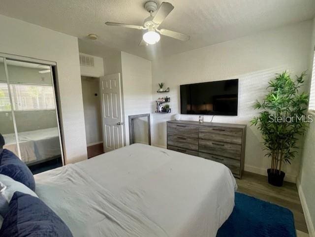 bedroom with ceiling fan, a textured ceiling, wood finished floors, visible vents, and baseboards