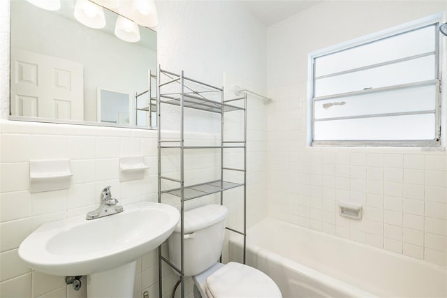 bathroom featuring washtub / shower combination, a sink, tile walls, and toilet