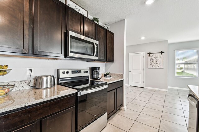 16126 Sunday Stroll Way, Odessa, FL 33556 - kitchen with stainless steel appliances, light tile patterned floors, dark brown cabinets, light stone counters, and baseboards