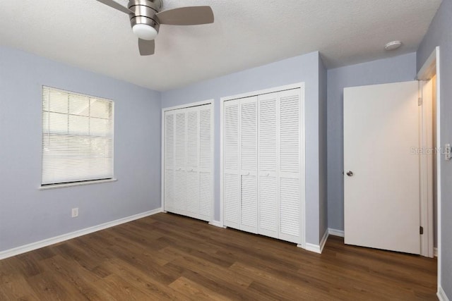 unfurnished bedroom with multiple closets, ceiling fan, a textured ceiling, and dark hardwood / wood-style flooring