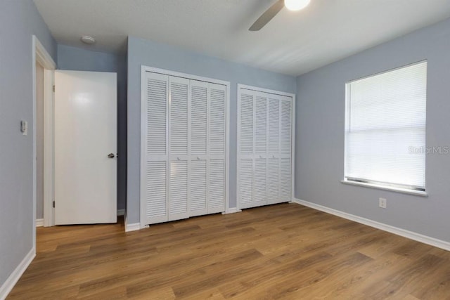 unfurnished bedroom with ceiling fan, light wood-type flooring, and two closets