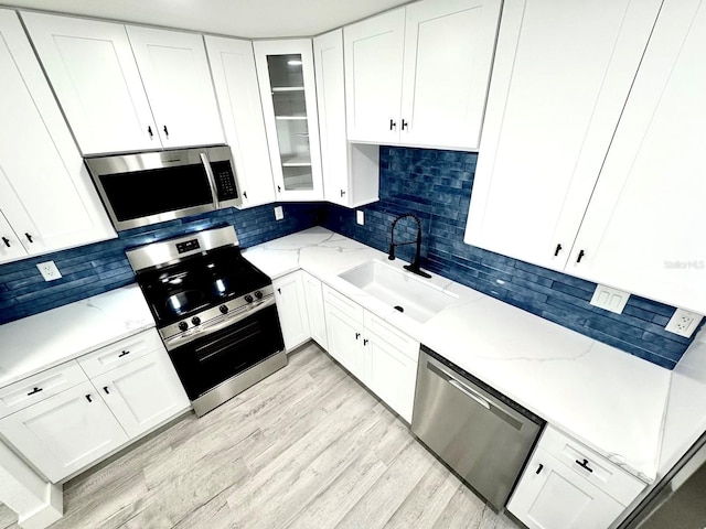 kitchen with light stone counters, stainless steel appliances, glass insert cabinets, white cabinetry, and a sink