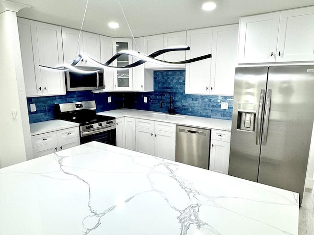 kitchen featuring stainless steel appliances, glass insert cabinets, white cabinetry, a sink, and light stone countertops