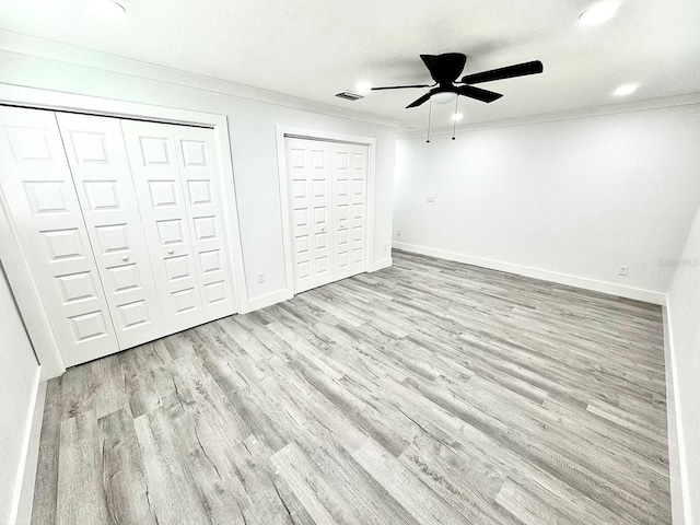 unfurnished bedroom featuring multiple closets, light wood finished floors, baseboards, and crown molding