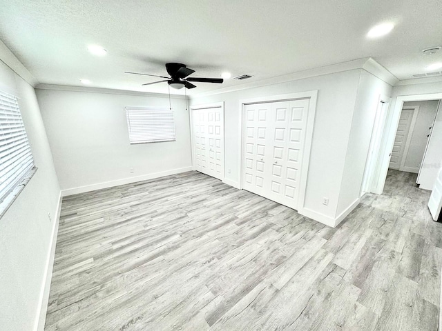 unfurnished bedroom with crown molding, multiple closets, light wood-style floors, a textured ceiling, and baseboards