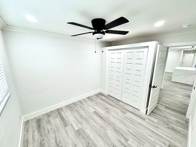 unfurnished bedroom featuring ceiling fan, light wood-style flooring, baseboards, ornamental molding, and a closet