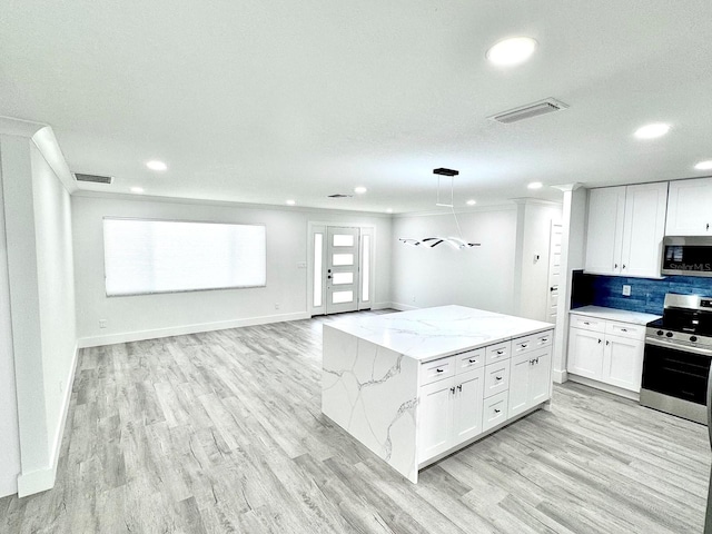 kitchen featuring open floor plan, appliances with stainless steel finishes, white cabinetry, and pendant lighting