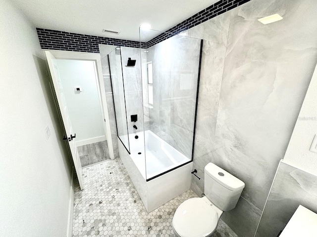 bathroom with tiled shower / bath combo, toilet, and tile walls