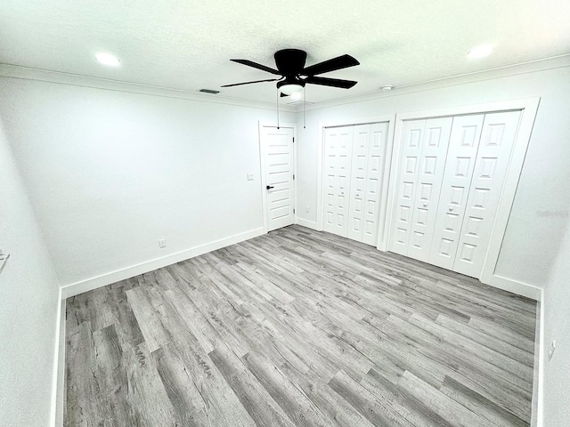 unfurnished bedroom featuring baseboards, two closets, light wood-style flooring, and crown molding