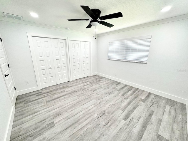 unfurnished bedroom with crown molding, multiple closets, visible vents, light wood-style flooring, and baseboards