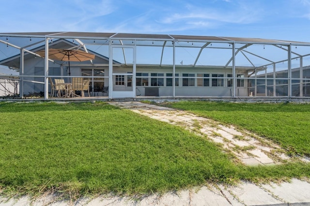 rear view of house featuring glass enclosure and a lawn