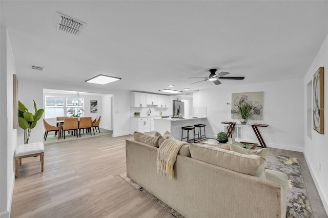 living room with sink, ceiling fan with notable chandelier, and light hardwood / wood-style flooring