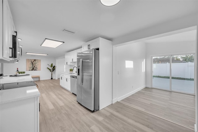 kitchen featuring appliances with stainless steel finishes, sink, light wood-type flooring, and white cabinets