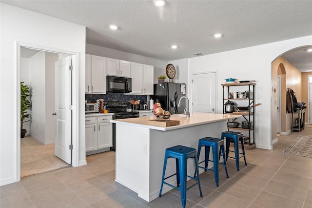 kitchen with a kitchen breakfast bar, white cabinetry, a kitchen island with sink, and black appliances