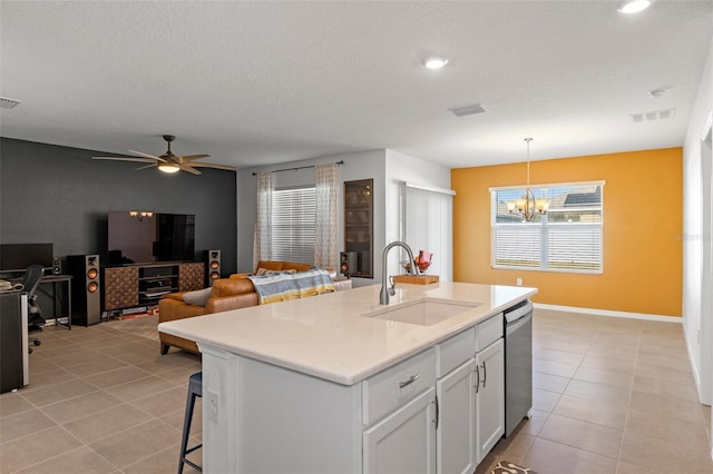 kitchen featuring a center island with sink, hanging light fixtures, stainless steel dishwasher, sink, and white cabinetry