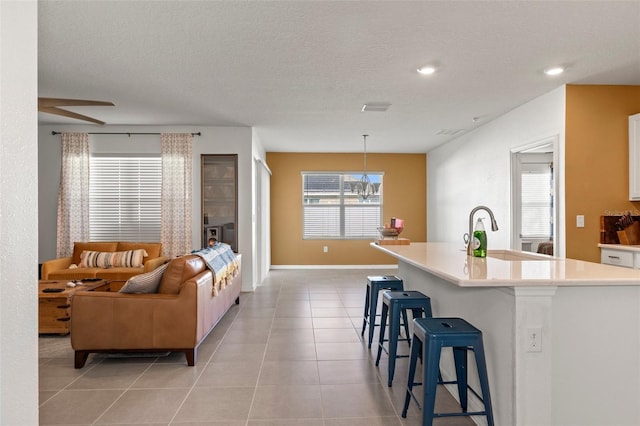 kitchen featuring a kitchen bar, light tile patterned floors, white cabinetry, decorative light fixtures, and a kitchen island with sink