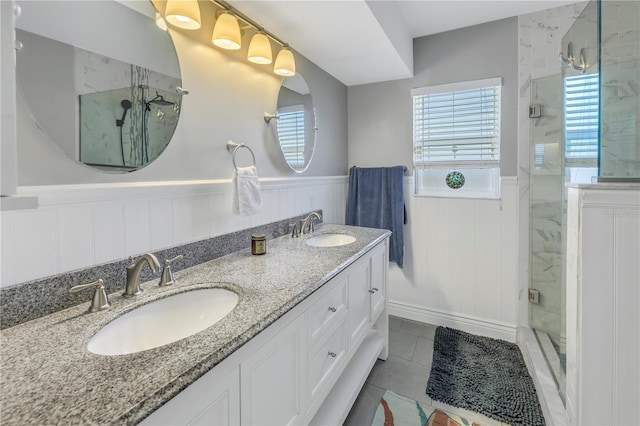 full bath with a wainscoted wall, double vanity, a sink, and a shower stall