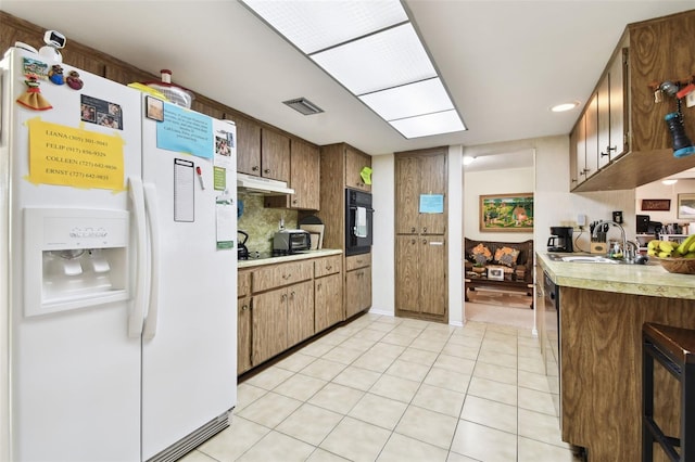 kitchen with sink, light tile patterned floors, black oven, white fridge with ice dispenser, and decorative backsplash