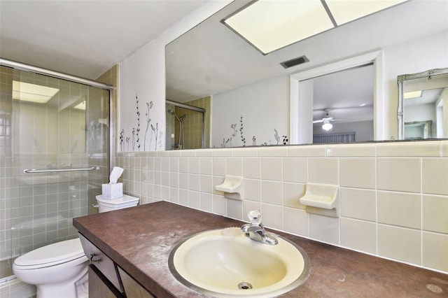 bathroom with toilet, an enclosed shower, tile walls, vanity, and ceiling fan