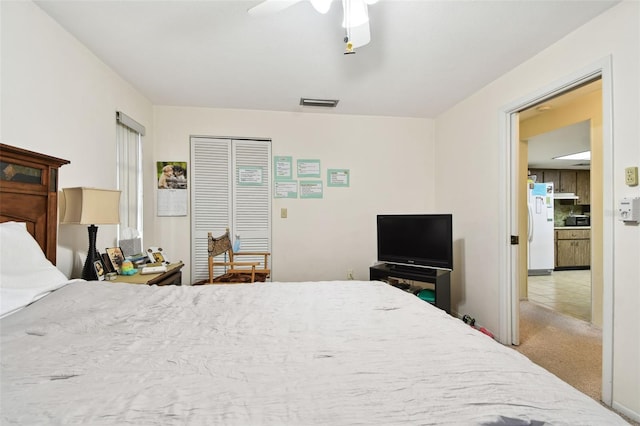 bedroom with white refrigerator, carpet flooring, ceiling fan, and a closet